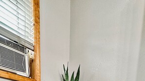 Une pièce d’angle avec une petite table et deux chaises, une plante en pot et une fenêtre avec des stores.