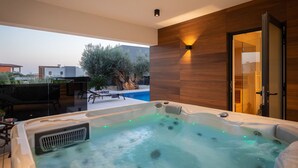 A modern outdoor hot tub area with a view of a swimming pool and a large tree. - Old Olive V by Interhome (Pula/Vodnjan)