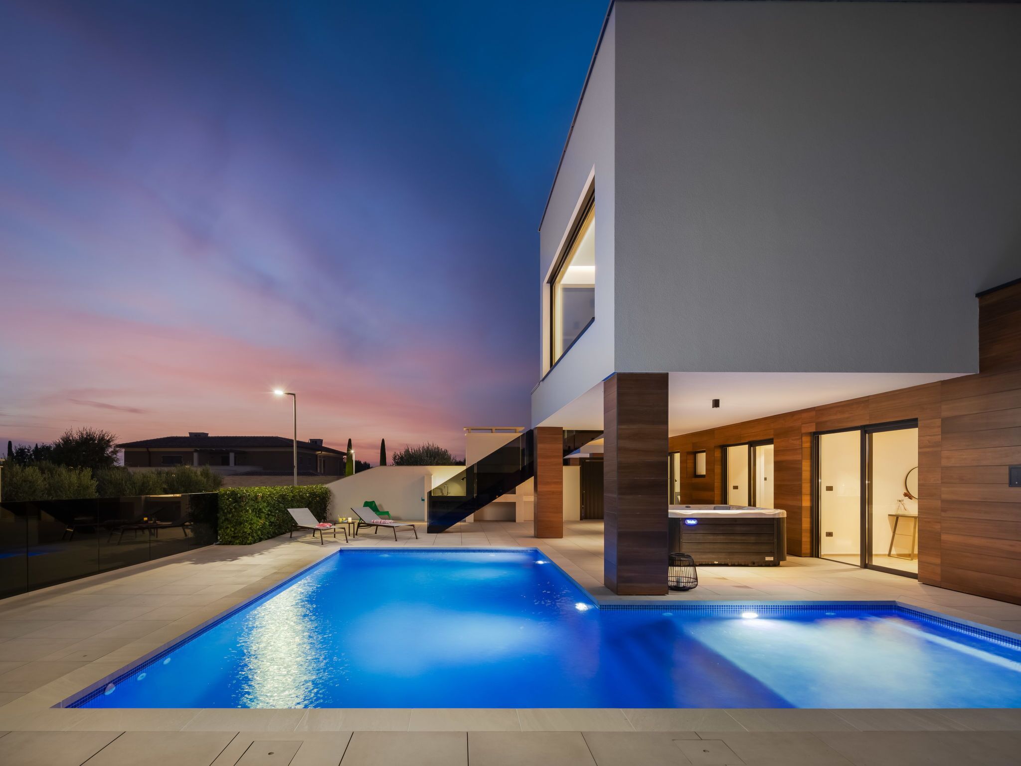 Una casa moderna con piscina, un área exterior cubierta y una escalera que conduce al piso superior.