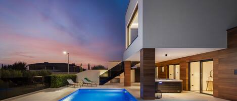 Una casa moderna con piscina, un área exterior cubierta y una escalera que conduce al piso superior.