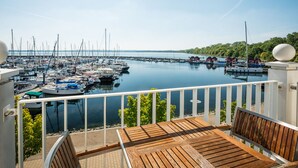 Un puerto deportivo con barcos amarrados, una terraza de madera con una mesa y sillas, y vistas al agua y la vegetación.