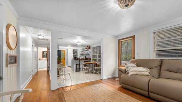 A spacious living room with a beige sofa, a wooden floor, and a kitchen area in the background.