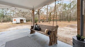 A wooden swing chair with cushions, a patterned rug, and a small shed in the background.
