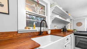 A kitchen with white cabinetry, a wooden countertop, a black faucet, and a window with decorative elements.