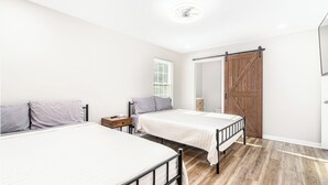 Ein Schlafzimmer mit zwei Betten, Holzboden, einer Schiebetür im Bauernhausstil und einem Deckenventilator.