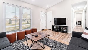 Ein modernes Wohnzimmer mit Couchtisch aus Holz, Teppich in Schwarzweißmuster und einem schwarzen TV-Schrank.