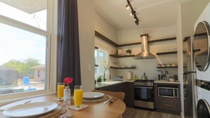 Cocina moderna con comedor, amplia ventana, electrodomésticos de acero inoxidable y espacio para el desayuno.