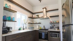 Una cocina moderna con armarios oscuros, electrodomésticos de acero inoxidable y estantes de madera.