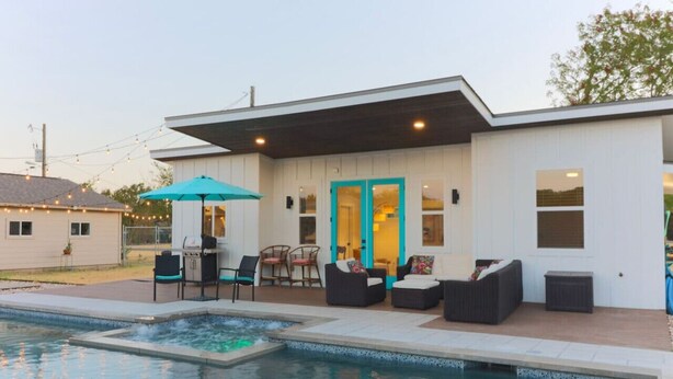 Una casa moderna con piscina, mobiliario exterior y un patio cubierto.