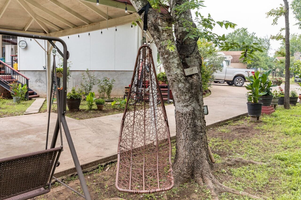 Un arbre avec une chaise suspendue, une balançoire et un bâtiment blanc en arrière-plan.