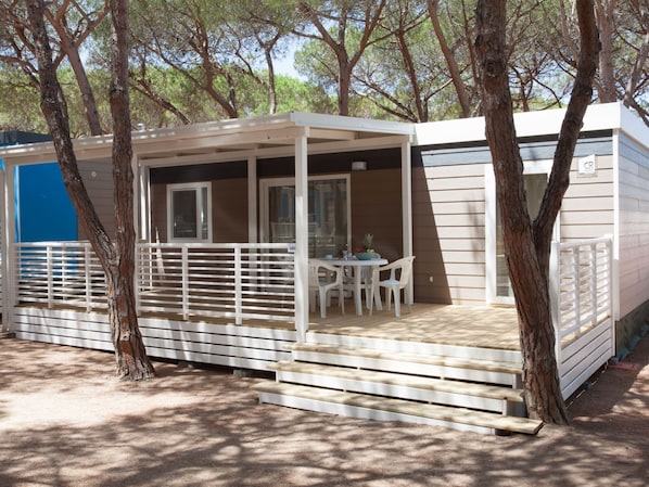 A mobile home with a covered patio area, a table with chairs, and a small deck.