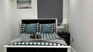 A neatly arranged bedroom with a checkered bedspread, two pillows, a bedside lamp, and a small nightstand with a lamp. - Studio - Sleeps 3 - Near Ealing Broadway Station (London)