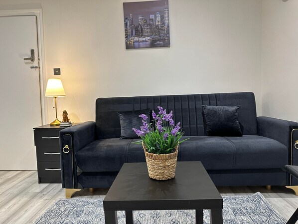 A modern living room with a dark blue sofa, a small table, a lamp, and a cityscape painting on the wall.