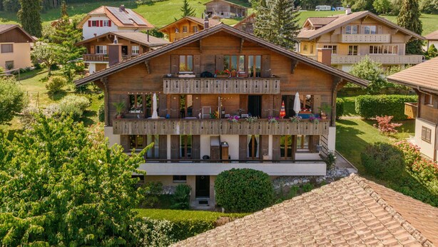A large wooden chalet with multiple balconies, surrounded by lush greenery and a mountainous backdrop. - Beatrice Garden by Interhome (Leissigen)