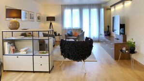 A modern living room with a sofa, a black chair, a coffee table, a TV, and a bookshelf. - Beatrice Garden by Interhome (Leissigen)
