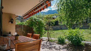 An outdoor patio with a wooden table and chairs, a pergola with climbing plants, and a view of mountains in the background. - Beatrice Garden by Interhome (Leissigen)