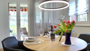 A dining area with a round wooden table, black chairs, a vase of tulips, and a modern pendant light. - Beatrice Garden by Interhome (Leissigen)