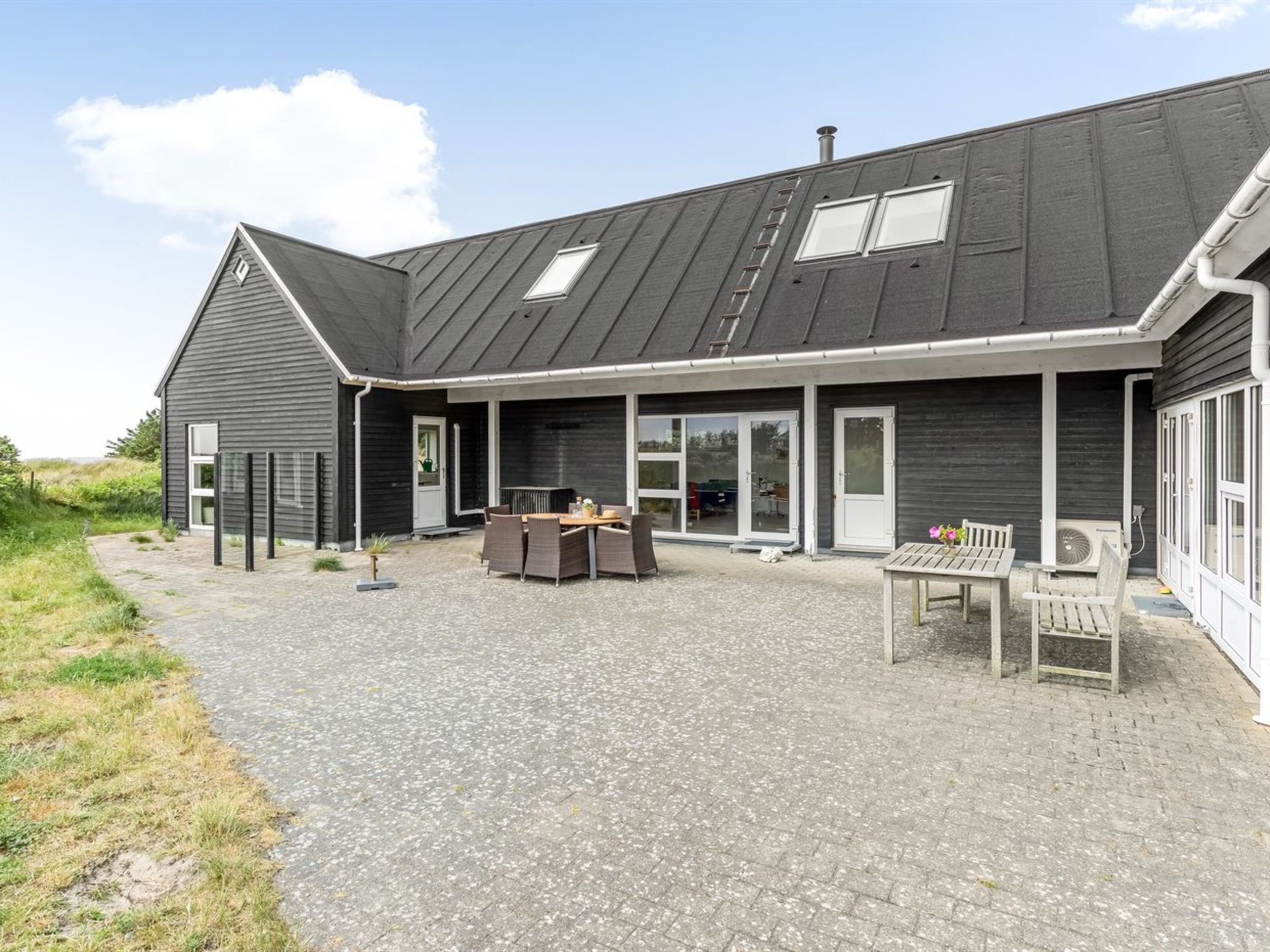Une maison moderne dotée d’un patio couvert, aménagé avec du mobilier d’extérieur et une table.