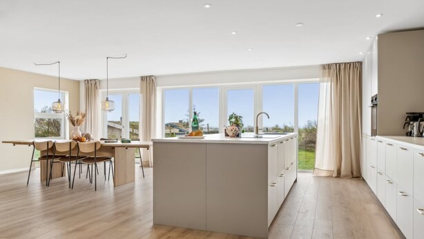 A modern kitchen with an island, large windows, and a dining area with chairs and a table.