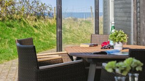 An outdoor seating area with wicker furniture, a table with books and a potted plant, and a view of the sea.