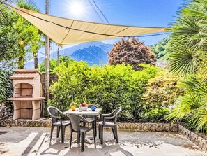 Une terrasse extérieure avec une table et des chaises, un four en pierre et un espace ombragé.