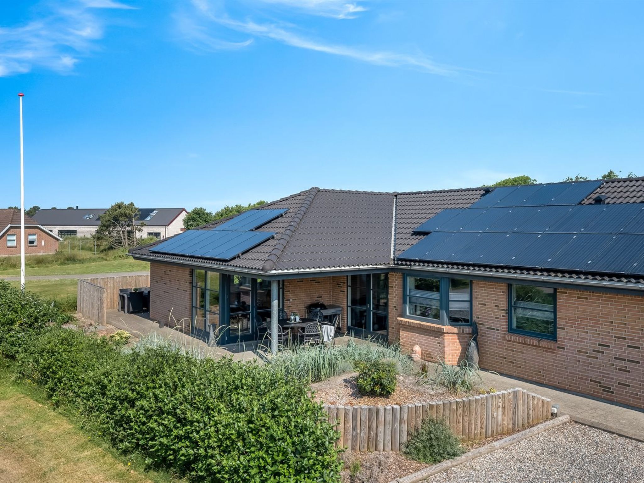 Een woongebouw met zonnepanelen op het dak, een overdekt terras en een verzorgde tuin.
