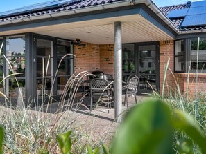Een overdekt terras met een bakstenen muur, glazen deuren en een tafel met stoelen.