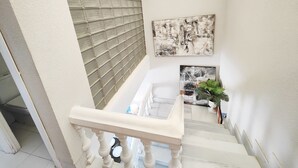 Un escalier avec une rampe blanche, un mur en blocs de verre et deux œuvres d’art abstraites.