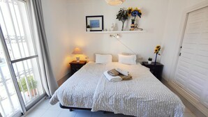Une chambre à coucher bien rangée, avec un lit, des tables de chevet, une lampe et une étagère ornée d’objets décoratifs.
