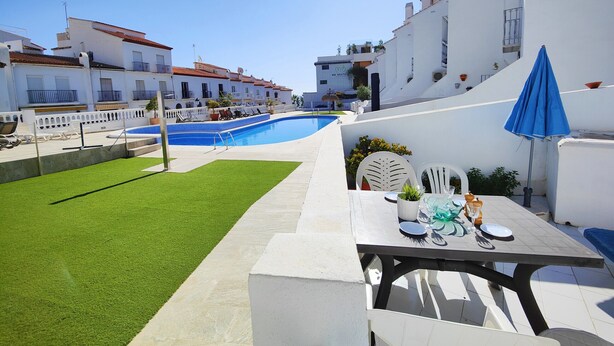 Une piscine entourée d’un ciel d’un bleu éclatant, un bâtiment blanc doté de balcons et une table avec des sièges pour l’extérieur.