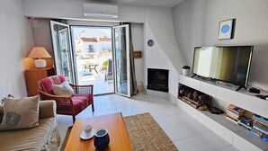 Un salon comprenant un canapé, une table basse, un téléviseur, une cheminée et donnant sur le balcon extérieur.