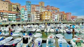 Un puerto deportivo con numerosas embarcaciones amarradas, un puente de piedra y edificios coloridos al fondo.
