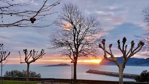 Un parque con una mesa de picnic, bancos y vistas al atardecer sobre un cuerpo de agua con montañas al fondo.