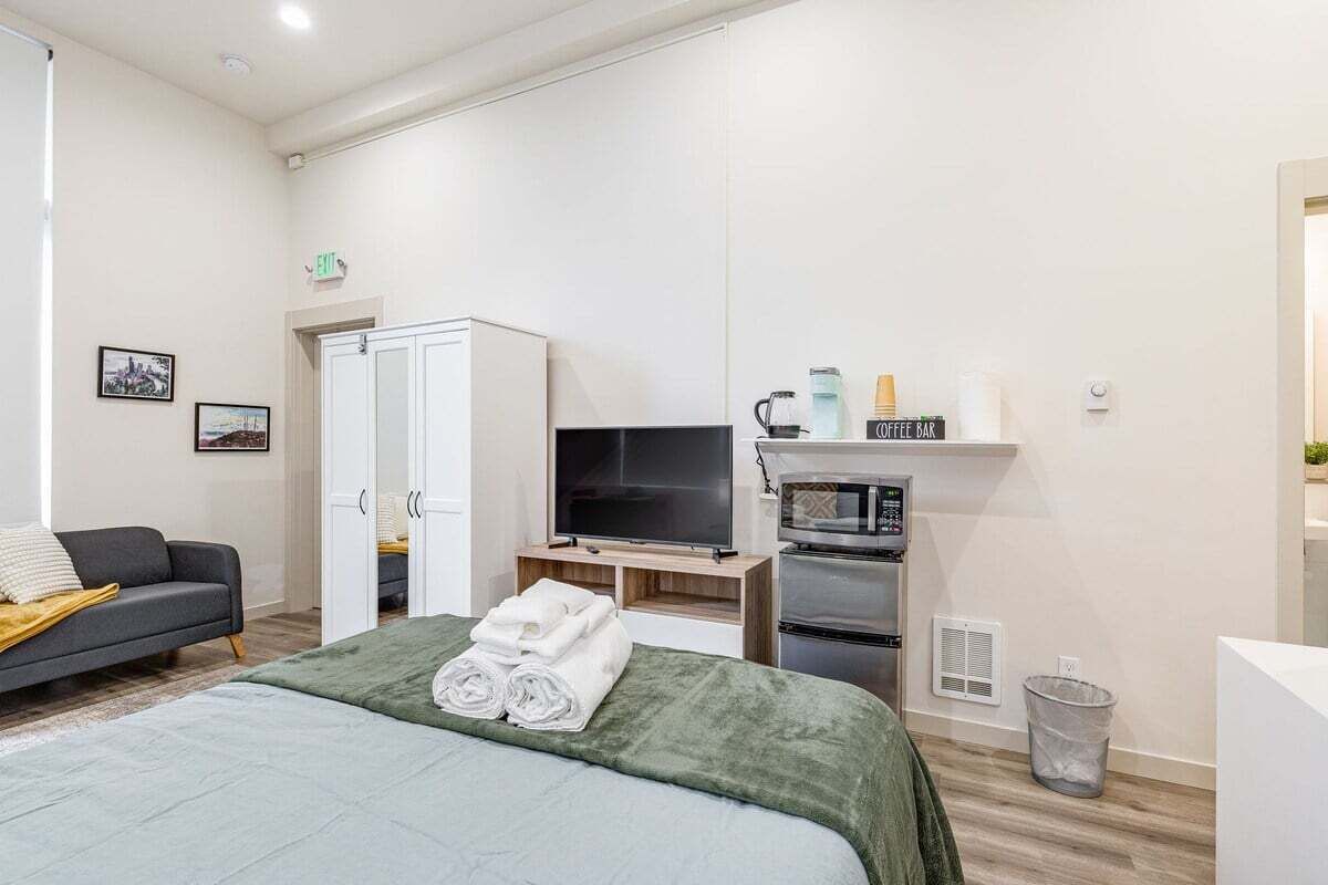 A modern hotel room with a bed, a television, a microwave, and a coffee bar.