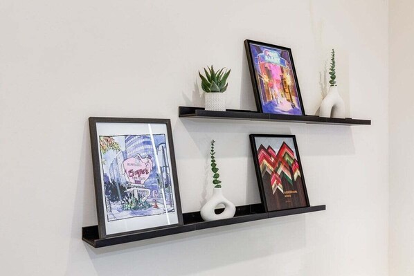 Dos estantes negros fijados a la pared, con obras de arte enmarcadas y jarrones decorativos.