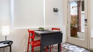 A modern room with a dining table, red chairs, a small side table with a lamp, and a door leading outside. - Perch - Cozy Studio | Own Bath | Heart of Fremont (Seattle)