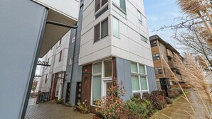 A modern multi-story building with a mix of glass and concrete facades, a visible entrance, and a small garden area with plants and a pathway. - Perch - Cozy Studio | Own Bath | Heart of Fremont (Seattle)