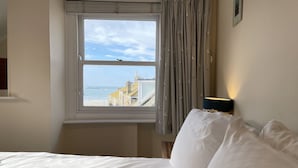 A hotel room with a bed, a window with a view of the beach and buildings, and a lamp on the bedside table.