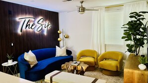 Un salon moderne avec un canapé bleu, des fauteuils jaunes, une table basse en bois et un panneau mural sur lequel on peut lire : « The Sip ».