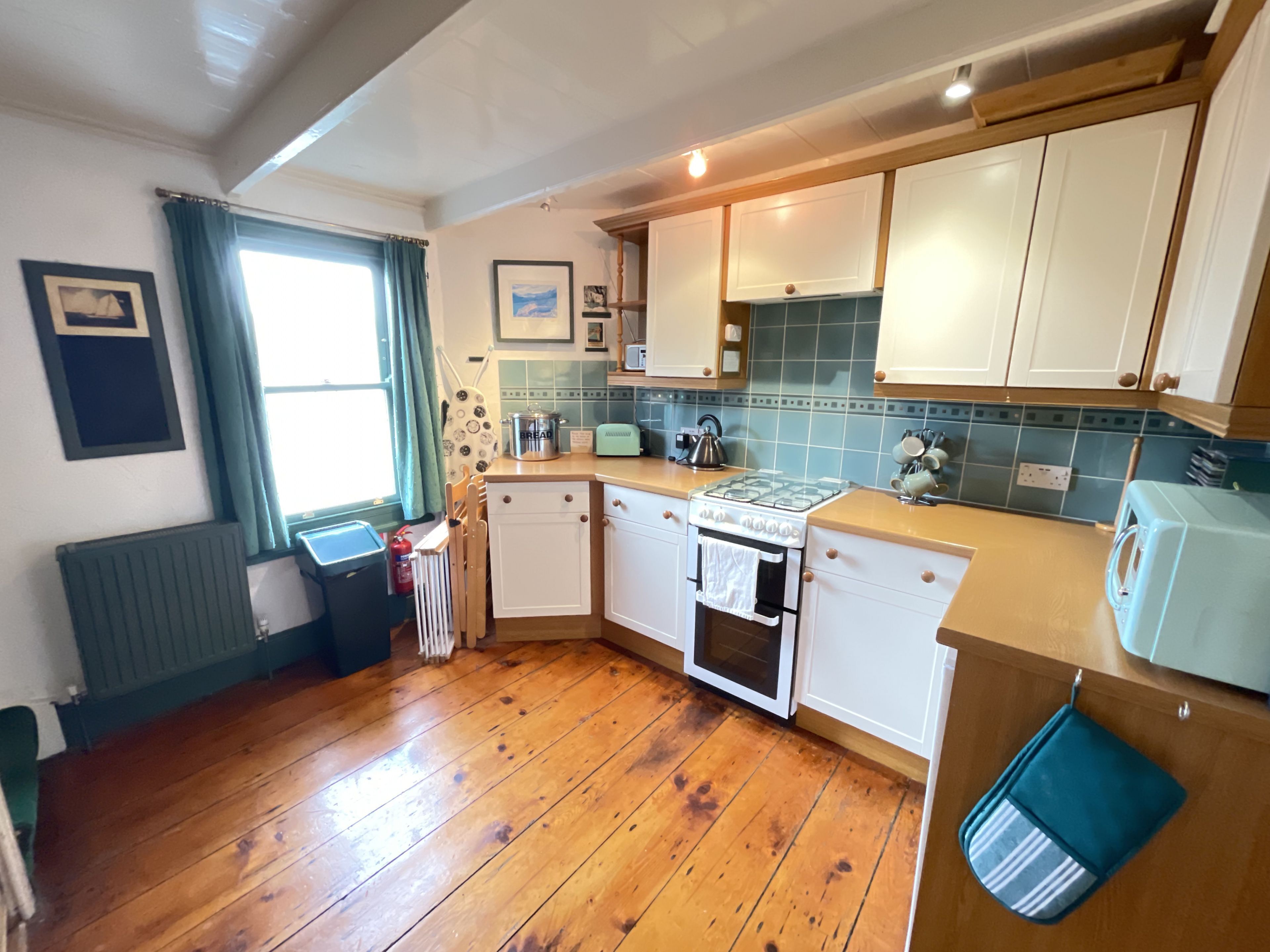 A kitchen with wooden flooring, white cabinets, a stove, and a toaster.