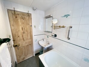 A bathroom with a wooden door, white tiles, a sink, a mirror, and a bathtub. - The Green House located on Upper Meadow (St Ives)