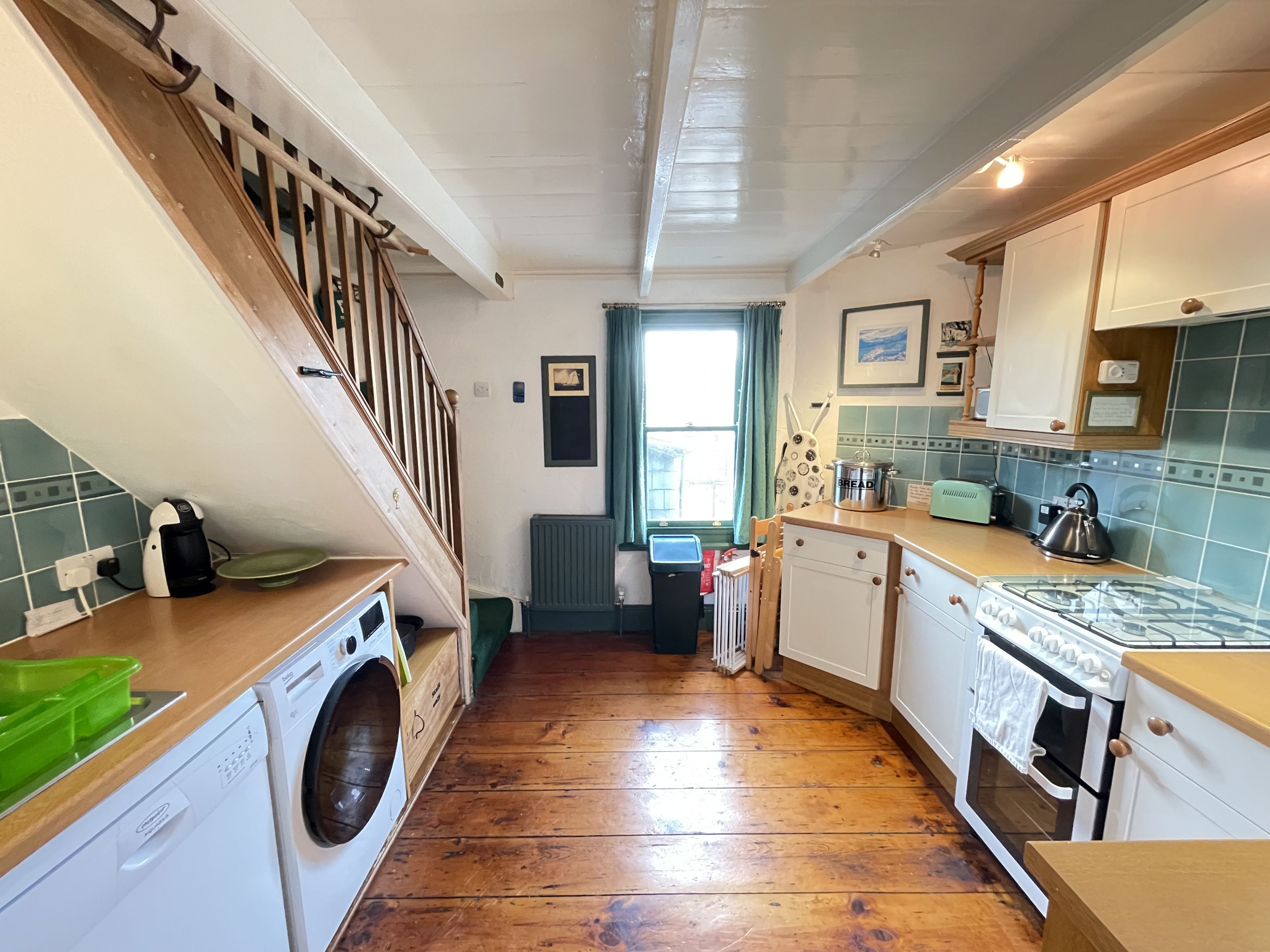 Cocina con suelo de madera, lavadora, estufa y ventana con cortinas.