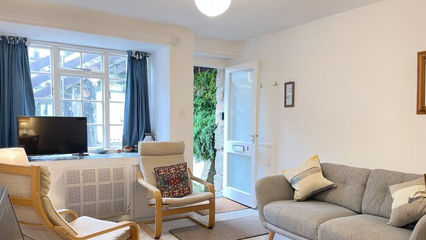 Un salon avec un canapé, un fauteuil, une télévision et une fenêtre avec des rideaux.