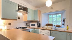 Une cuisine avec des meubles de couleur bleu clair, un plan de travail en bois, un four à micro-ondes, un grille-pain, une cuisinière, un évier et une fenêtre donnant sur un paysage verdoyant.