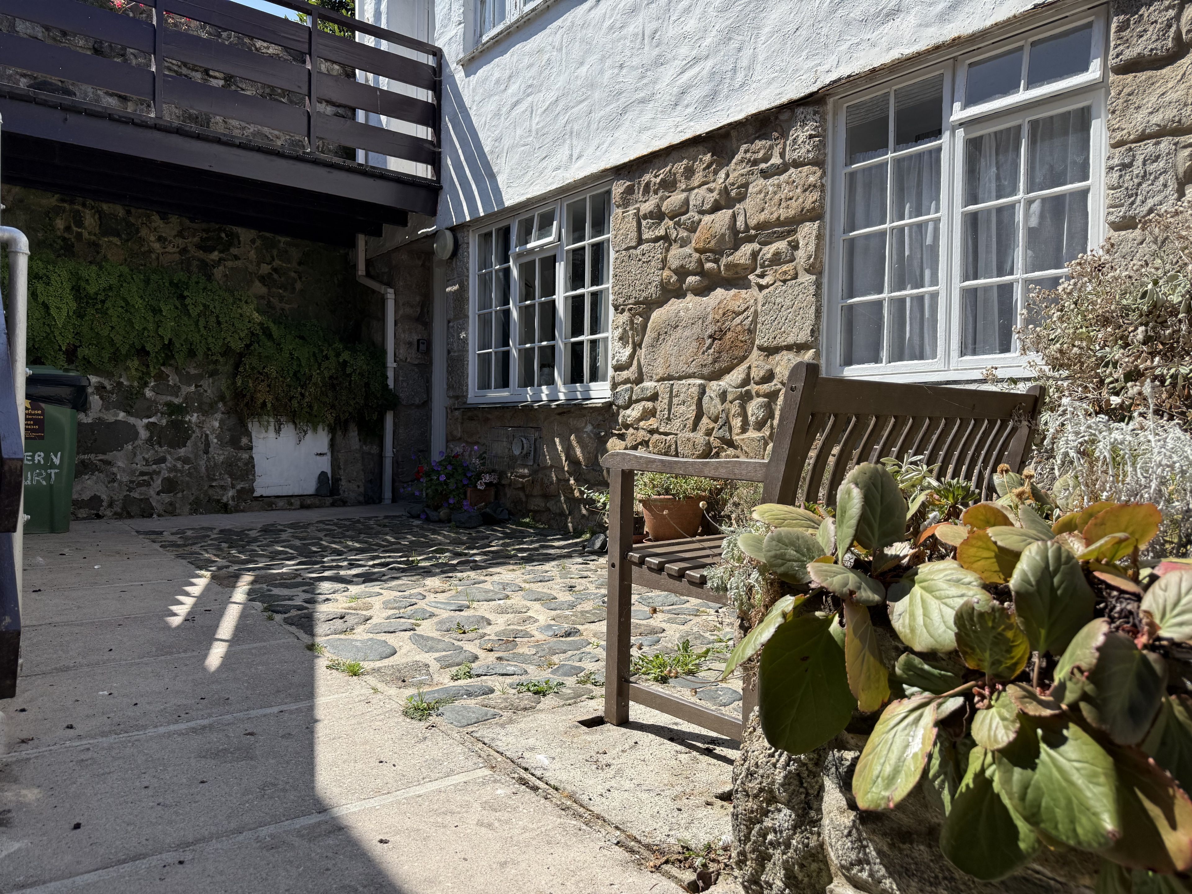 A stone building with a bench, a potted plant, and a trash bin.