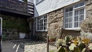 Un bâtiment en pierre avec un banc, un pot de fleurs et une poubelle.
