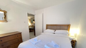Un lit bien fait, avec du linge de lit et des serviettes blanches, une commode en bois et une tête de lit en bois.