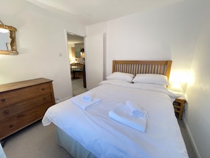 A neatly made bed with white linens and towels, a wooden dresser, and a wooden headboard.