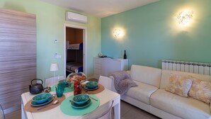 Un salon comprenant un canapé, une table à manger avec de l’assiette et une bouilloire, ainsi qu’un luminaire fixé au mur.