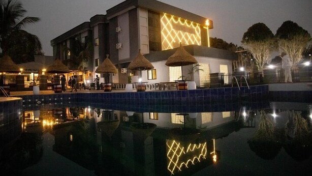 Un hotel amb piscina, mobiliari exterior amb sobreadors de palla i una façana moderna amb dibuixos il·luminats.